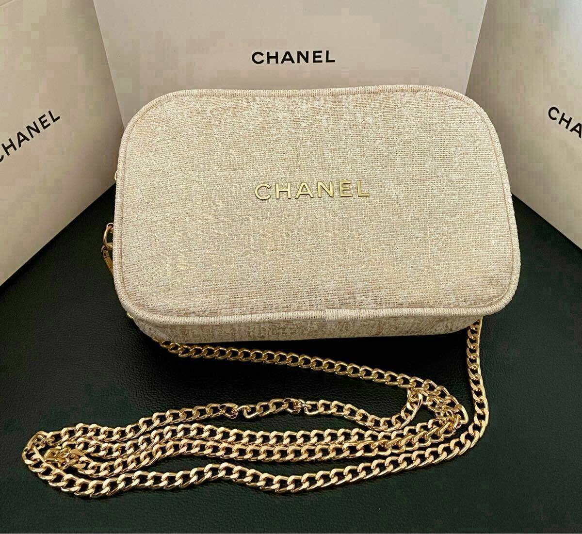 Beige glitter Chanel canvas pouch with gold CHANEL logo and a gold chain strap shown on a dark surface with Chanel boxes behind it.
