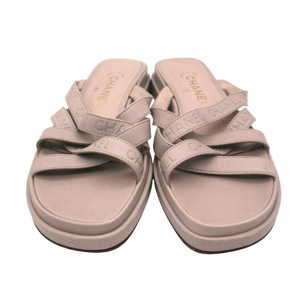 Front view of a pair of CHANEL greyish-green leather sandals with crossed logo straps.