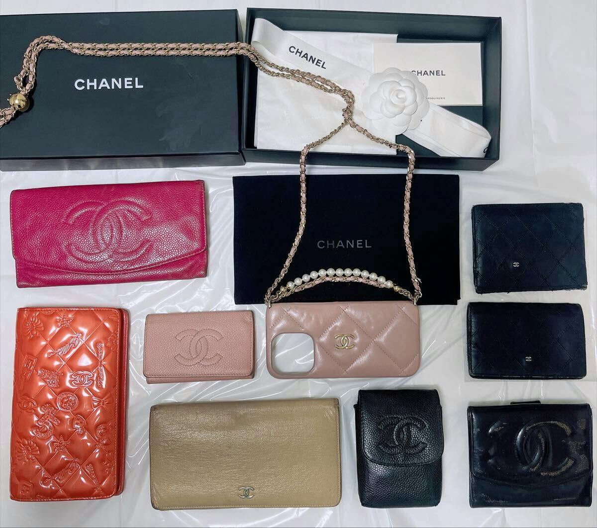 Overhead view of multiple CHANEL wallets and small leather goods, including a pink quilted phone case with chain and branded boxes on a white surface.