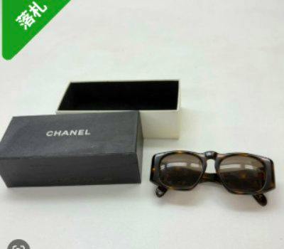 CHANEL tortoiseshell plastic sunglasses displayed next to their box on a white surface.