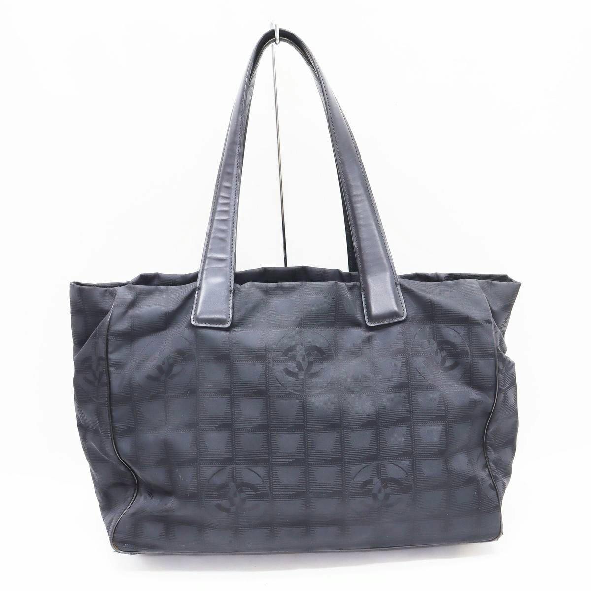 Front view of a black CHANEL New Travel Line canvas tote bag with shoulder straps and repeating CC motif.