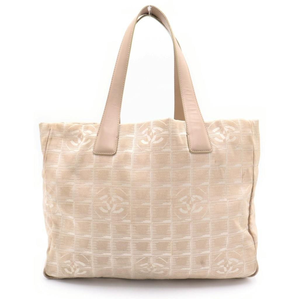 Front view of a beige CHANEL New Travel Line canvas tote bag showing the Coco mark pattern and leather handles.