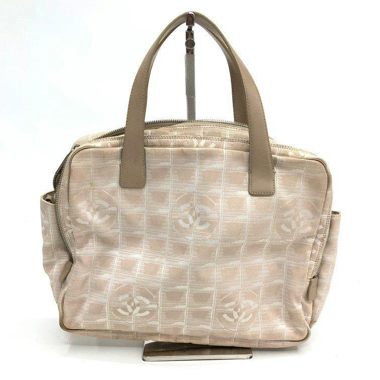 Front view of the CHANEL New Travel Line canvas handbag in beige with a grid pattern and interlocking CC motifs, leather handles and a side pocket.