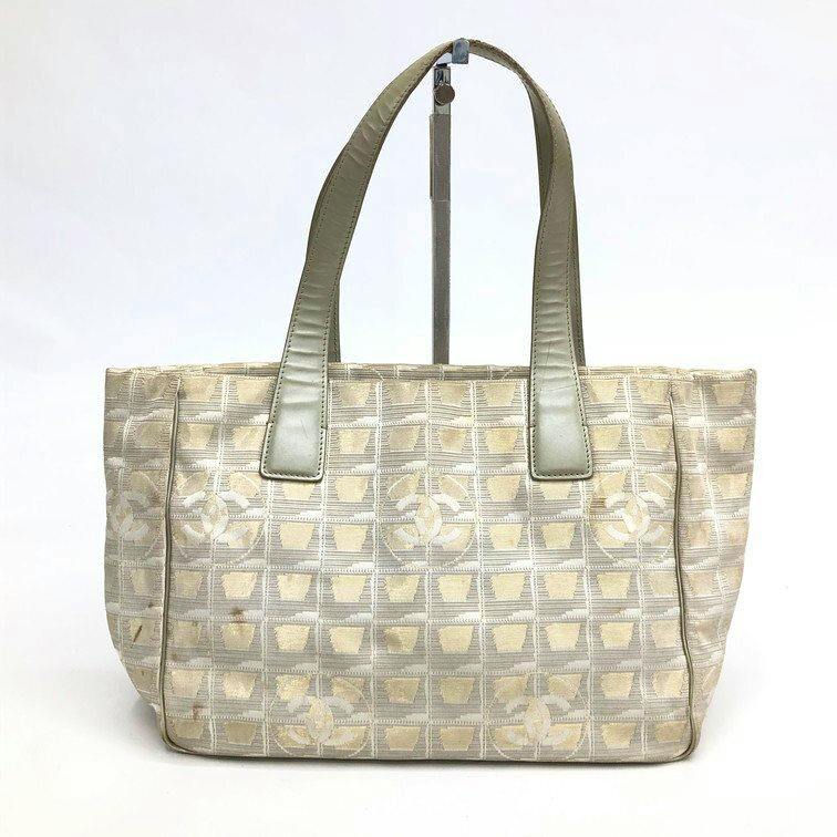 Front view of the CHANEL canvas tote bag showing the grid pattern with Coco logos and leather shoulder handles.