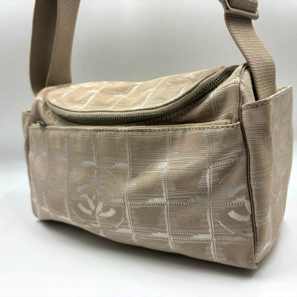Beige CHANEL New Travel Line shoulder/camera bag in jacquard canvas shown from a side angle, displaying the adjustable strap and exterior front pocket.