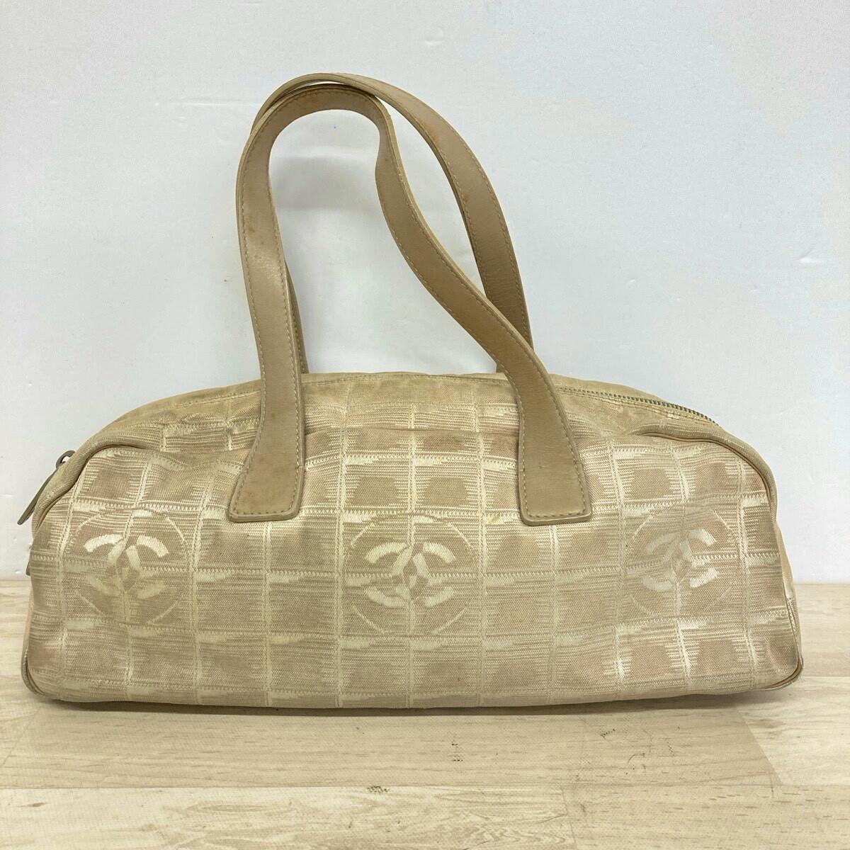 Front view of a beige CHANEL New Travel Line mini boston handbag in canvas showing dual top handles and a repeating CC motif.