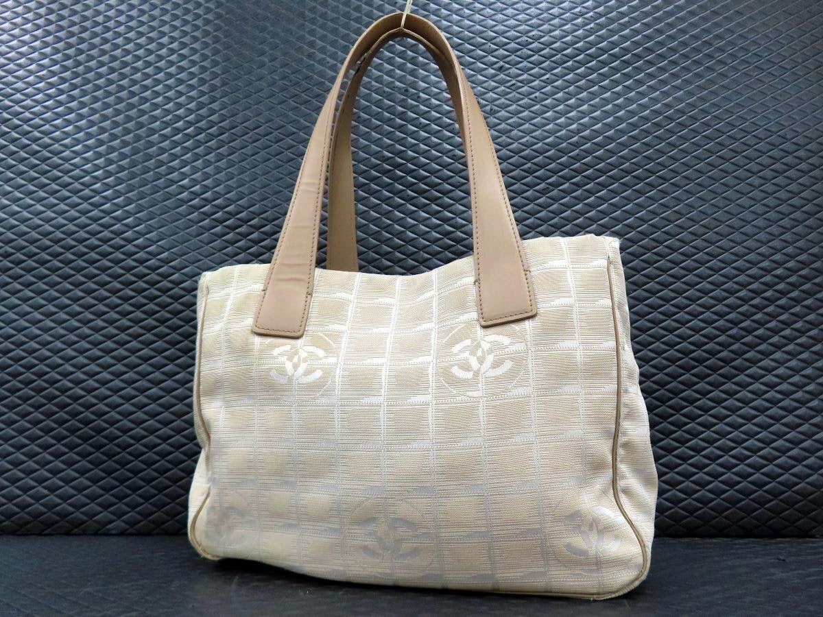 Beige CHANEL New Travel Line nylon and calf leather tote bag with double top handles and repeating Coco logo pattern shown from the front.