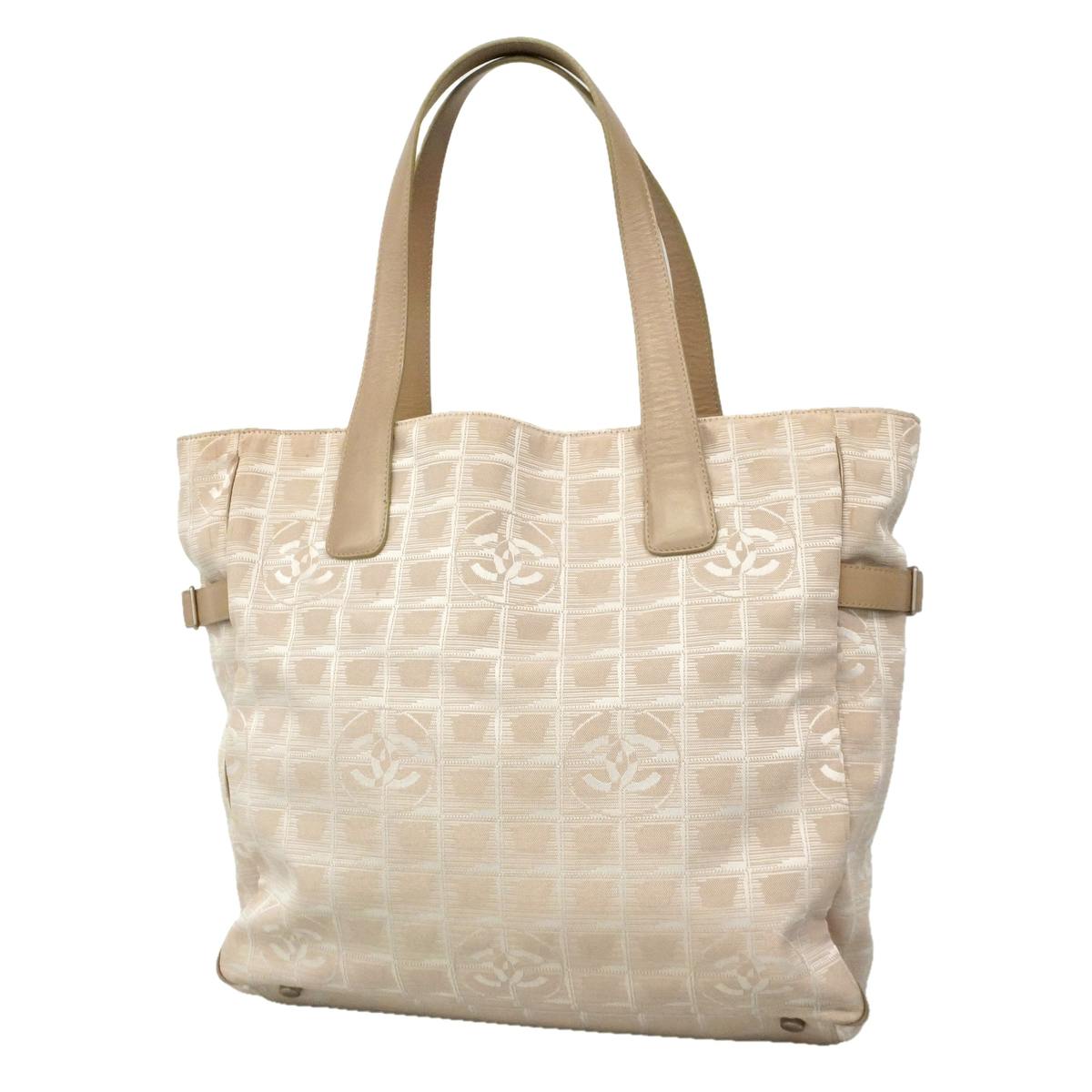 Front view of a beige CHANEL New Travel nylon canvas tote bag with beige leather handles and silver hardware.