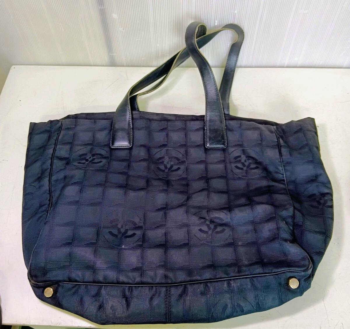 Black CHANEL New Travel Line nylon tote bag with leather handles and repeating CC pattern, shown laid flat.
