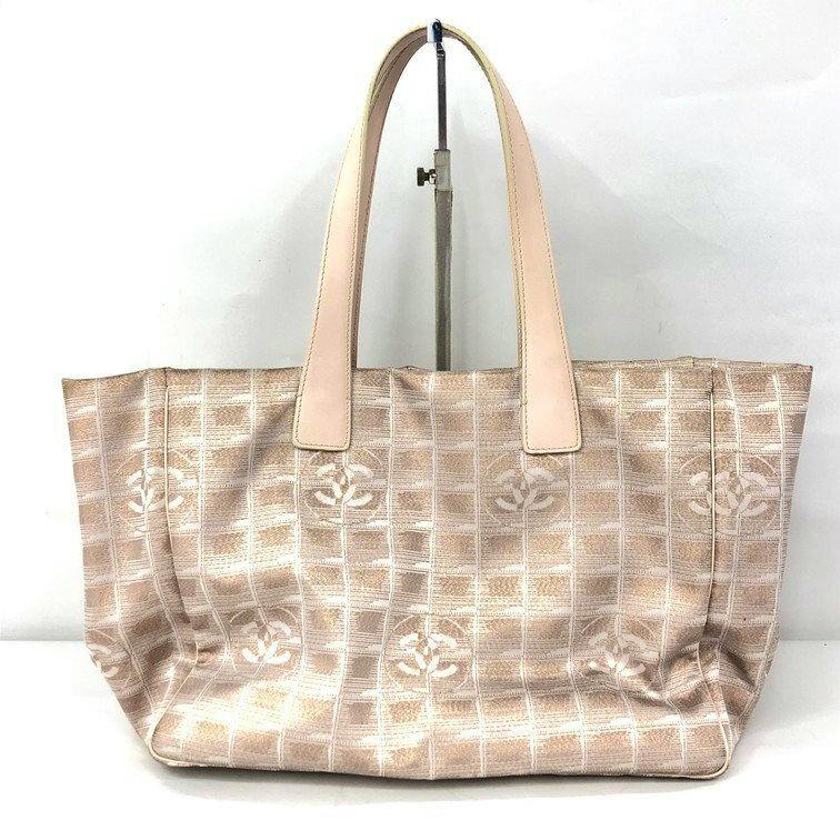 Front view of a CHANEL New Travel Line nylon tote bag with light leather handles and a repeating CC logo grid pattern on beige fabric.