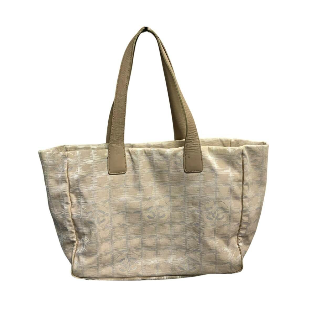 Front view of a beige Chanel New Travel Line nylon jacquard tote bag with beige leather handles.