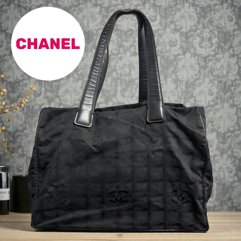 Front view of a black CHANEL New Travel Line nylon tote bag with two shoulder handles.