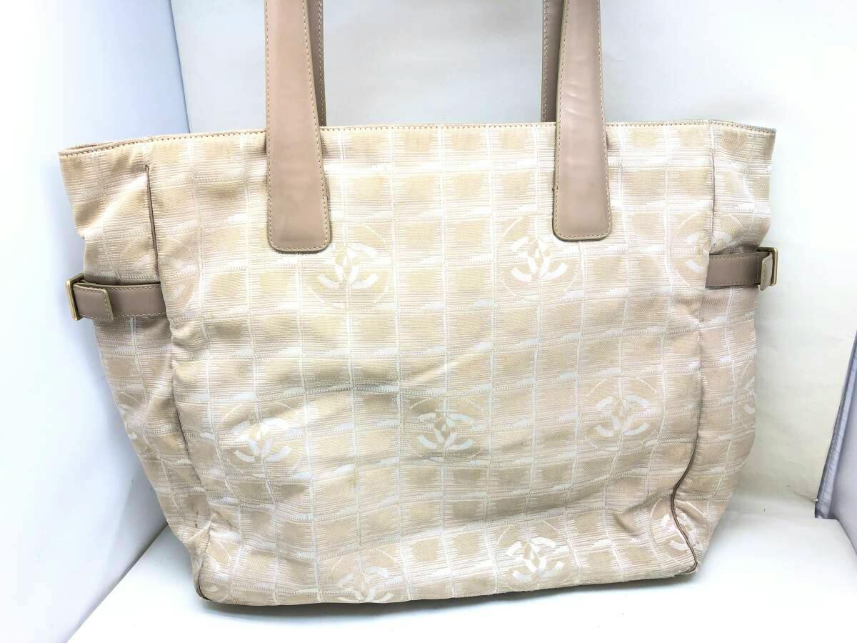 Front view of a beige CHANEL New Travel Line canvas tote GM with shoulder straps and repeating CC logo pattern.