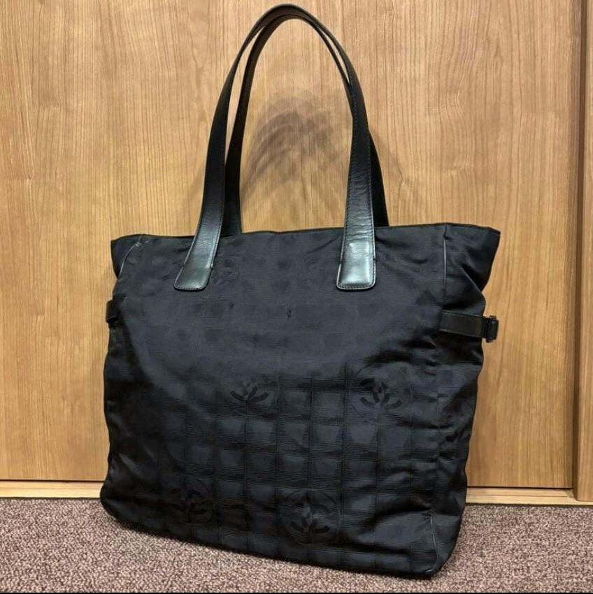 Front view of the black CHANEL nylon New Travel Line Tote GM bag with leather shoulder handles against a wooden background.