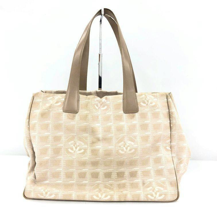 Front view of a beige CHANEL New Travel Line MM canvas tote bag with leather handles on a white background.