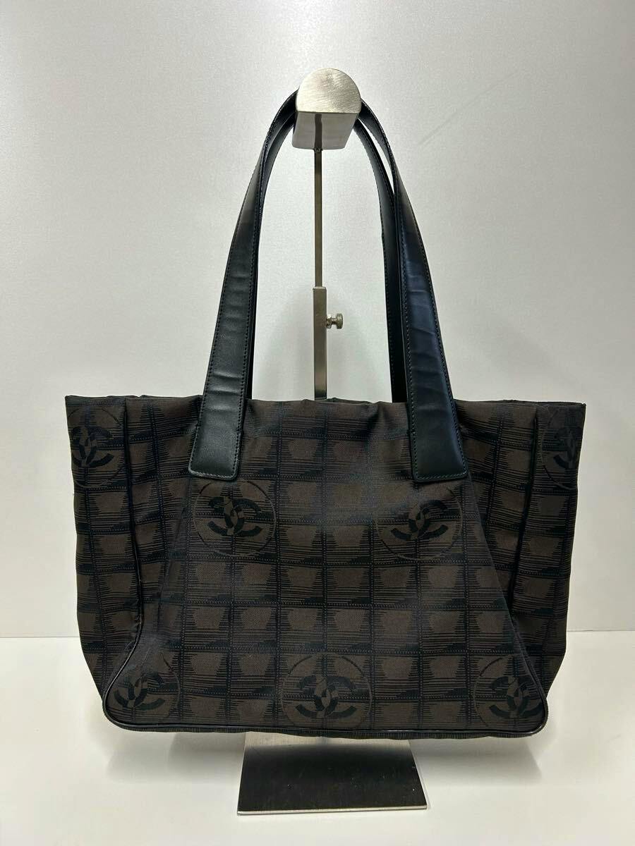 Front view of a CHANEL New Travel Line PM nylon tote bag with dark patterned fabric and leather handles on a display stand.