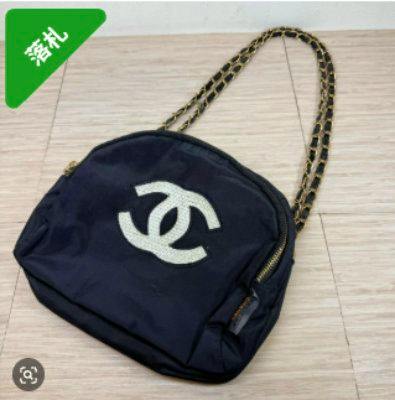 Black Chanel novelty shoulder bag with white interlocking CC logo, chain-link shoulder strap, and nylon exterior placed on a light-colored floor.