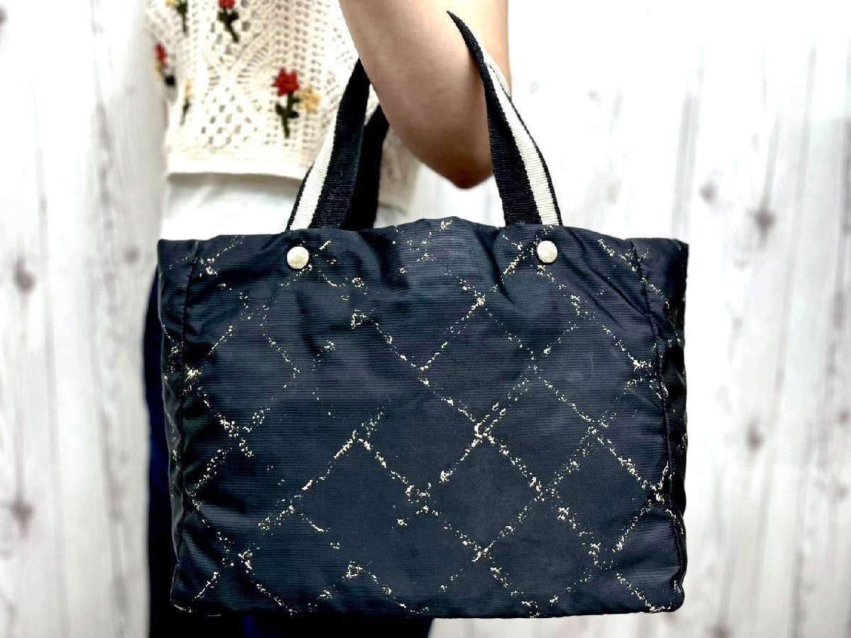 Black CHANEL nylon and canvas tote bag with a diamond quilted pattern held by a person.