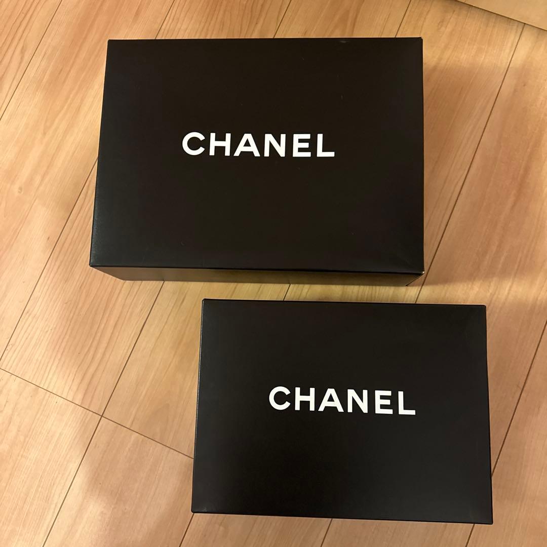 Two black Chanel paper boxes with white "CHANEL" logos placed on a wooden floor.