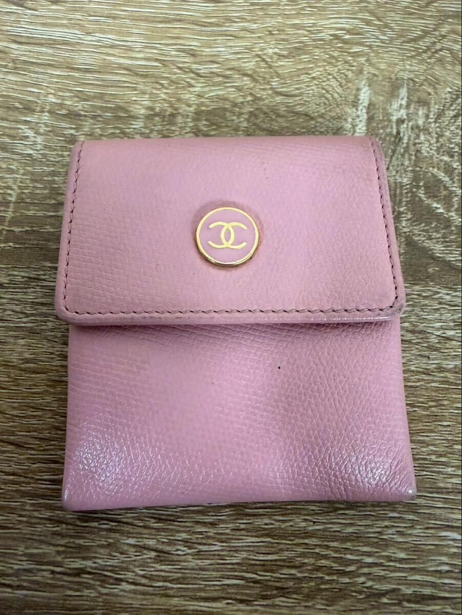 Pink Chanel leather coin case with a gold CC logo on the flap on a wood surface.