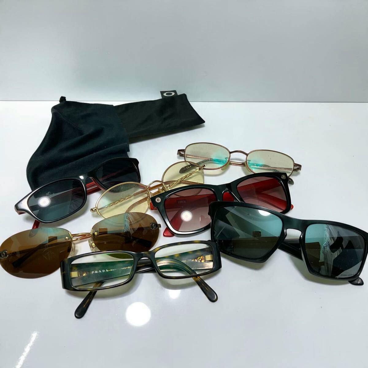 Seven pairs of sunglasses of various styles arranged on a white surface with a black soft pouch.