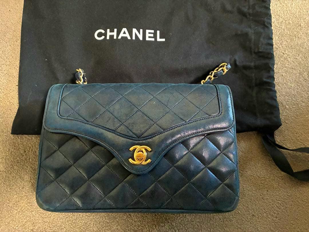 Front view of a quilted lambskin Chanel flap bag with a gold CC turn-lock and double chain, shown on a Chanel dust bag.