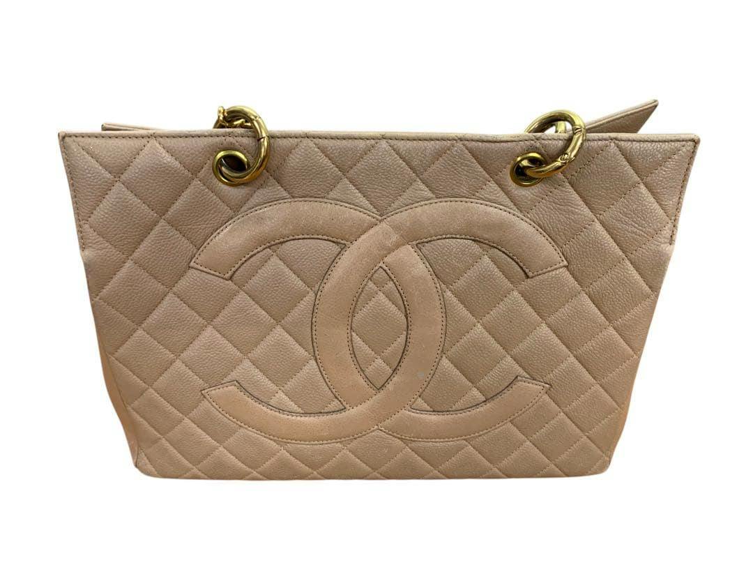 Front view of a beige CHANEL caviar leather quilted tote bag showing a large interlocking CC logo and gold-tone chain hardware.