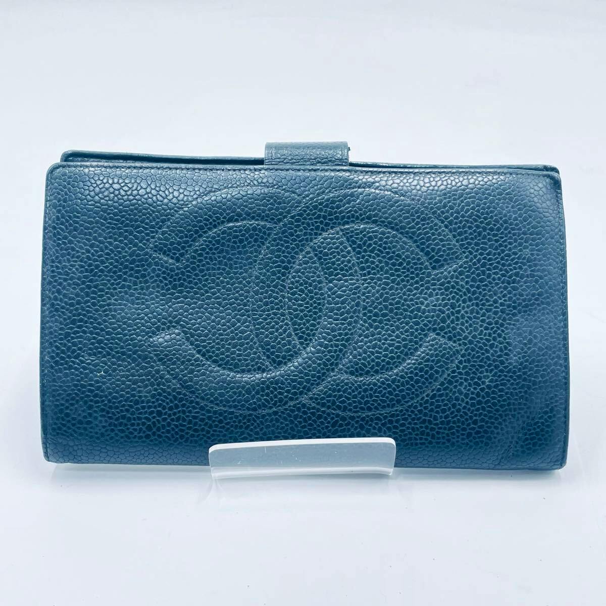 Closed CHANEL cow leather long wallet with a large embossed interlocking CC on the front, shown on a clear stand.