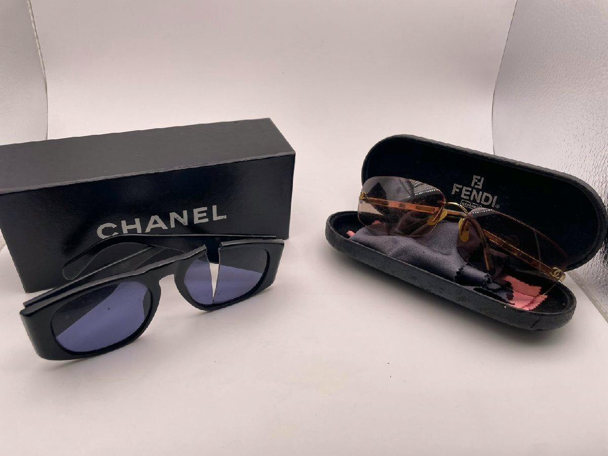 Two sunglasses displayed on a white background with a black CHANEL box on the left and an open FENDI case on the right.