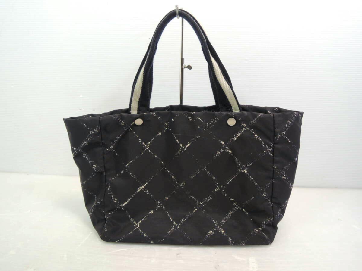 Front view of a black nylon Chanel tote bag with a quilted diamond pattern and striped handles displayed on a stand.