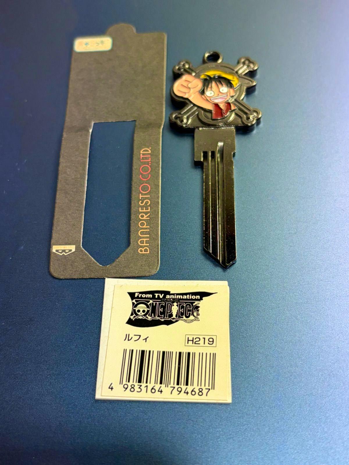 Metal car key cover featuring Luffy from One Piece attached to a key blade, shown with its cardboard tag and barcode on a blue surface.