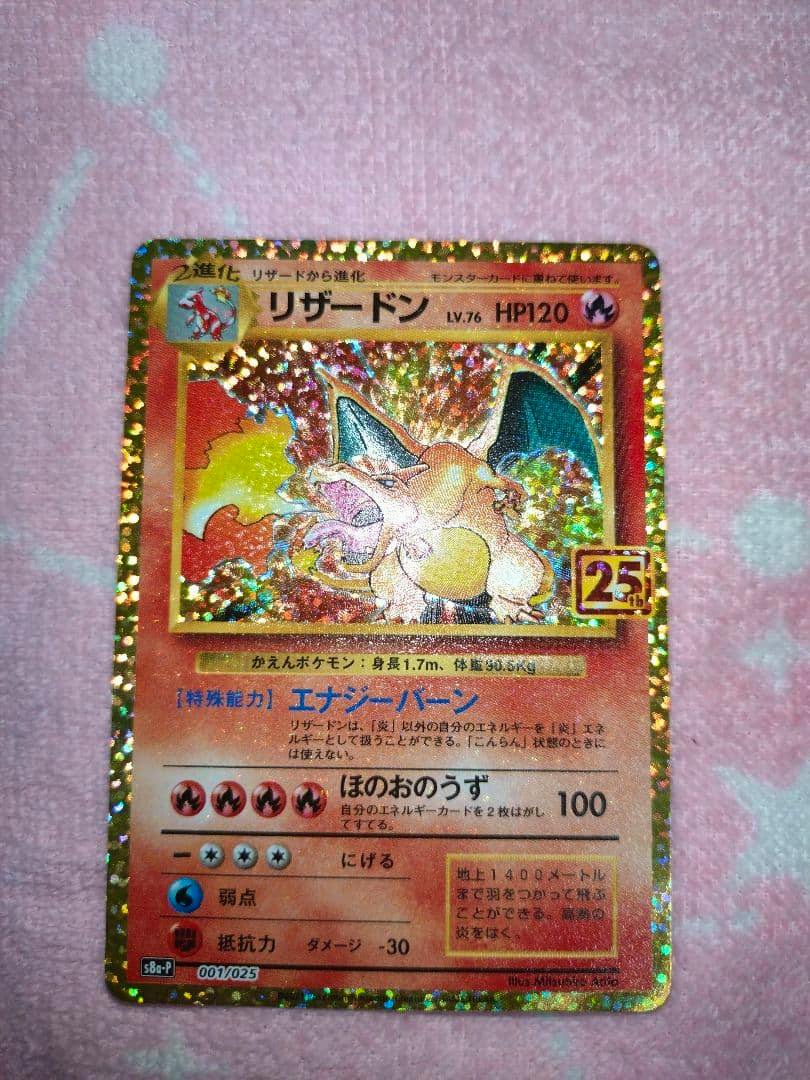 Photograph of the リザードン 25th holographic promo trading card on a pink fabric background.