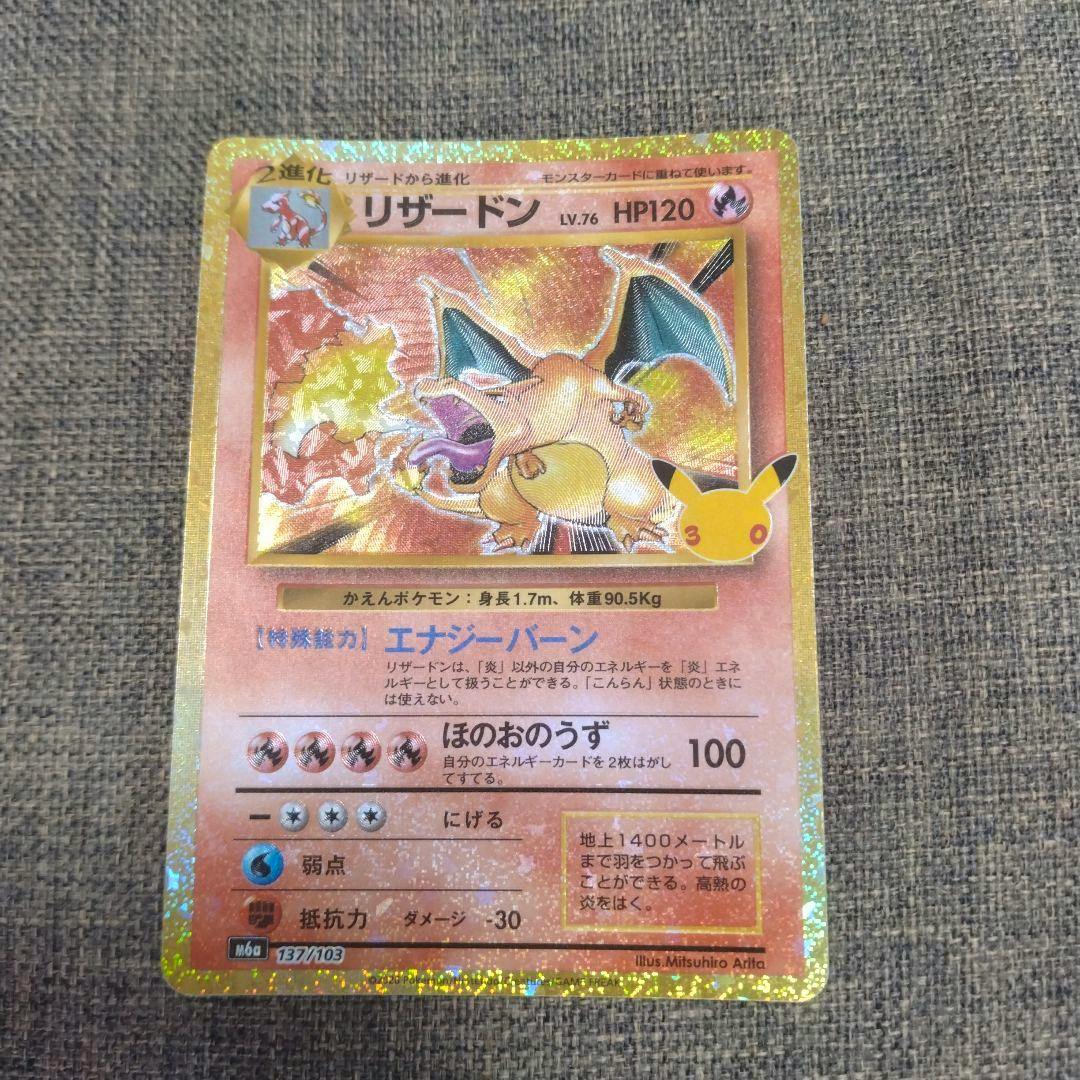 Front of a holographic Japanese リザードン (Charizard) Pokémon trading card showing the artwork, text, and stats on a fabric background.