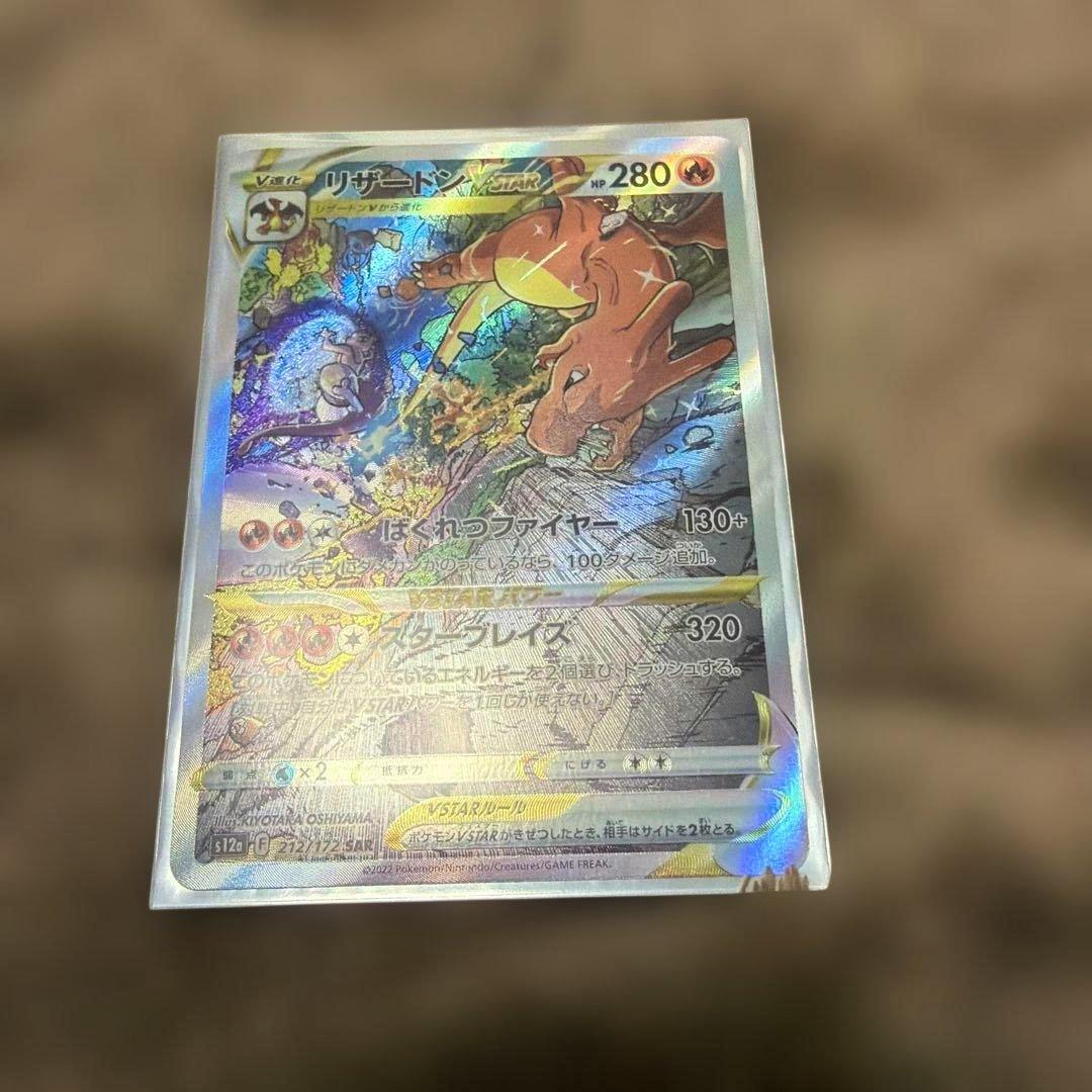 Holographic リザードン VSTAR trading card in a plastic sleeve photographed against a blurred brown background.