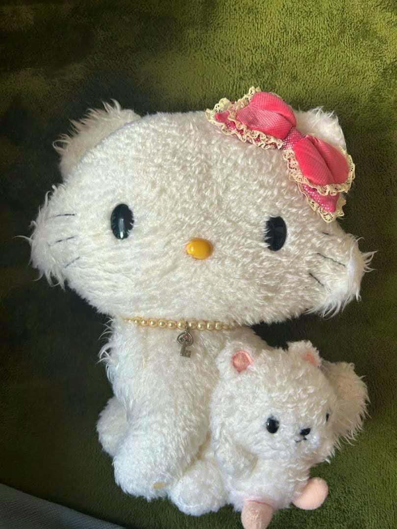 Front view of a white Charmmy Kitty plush with a pink bow and pearl necklace holding a small white stuffed animal.