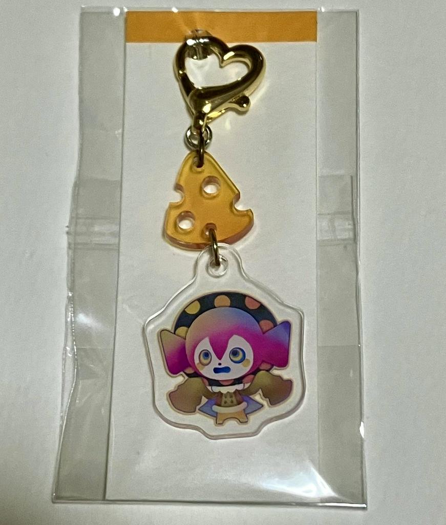 Photo of the acrylic keychain charm with a gold heart clasp, a cheese-shaped connector, and a colorful character charm inside clear plastic packaging.