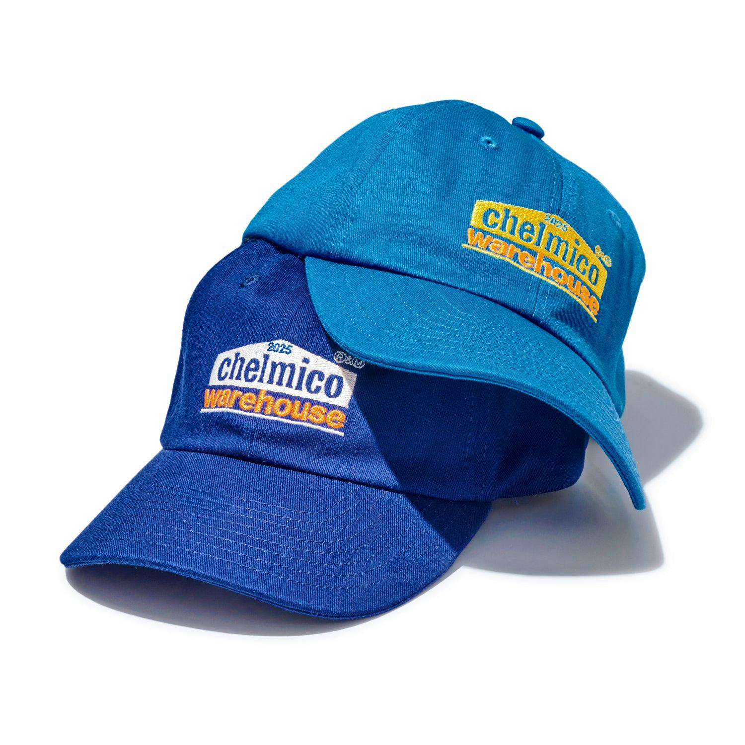Two chelmico warehouse baseball caps in different blue shades stacked, showing the embroidered "chelmico warehouse" logo.