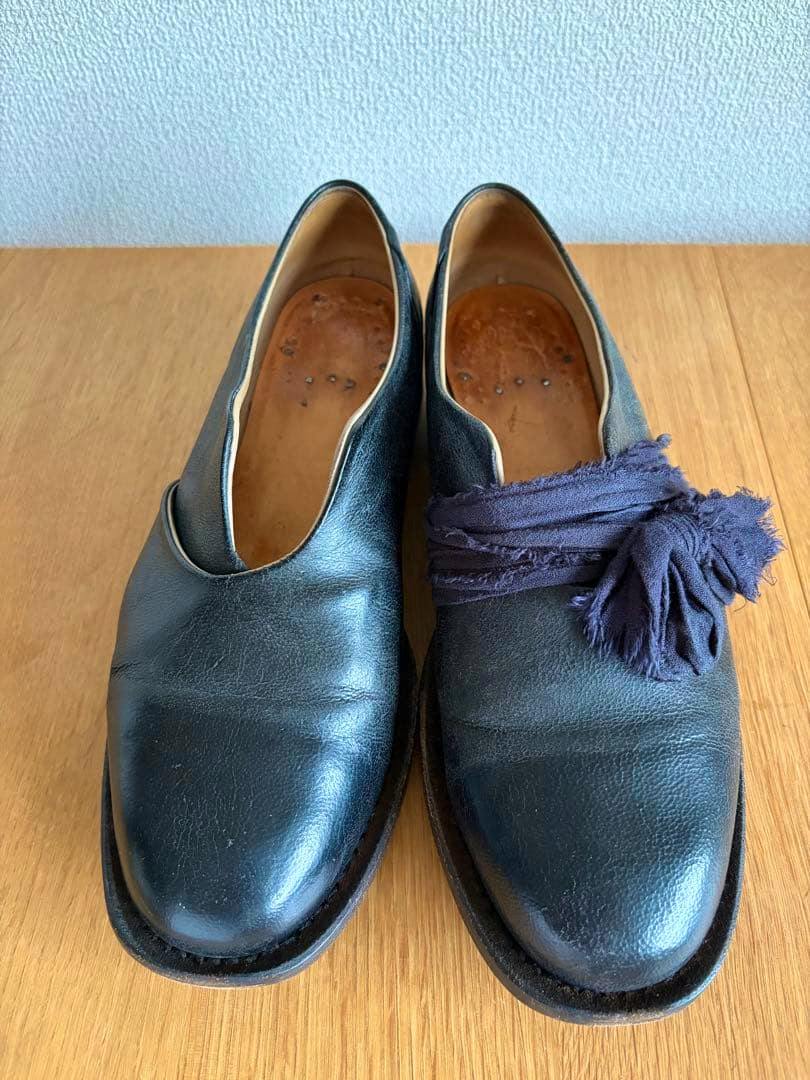 Top view of a pair of black leather derby-style shoes (size 38) on a wooden surface, the right shoe wrapped with a fabric strip.