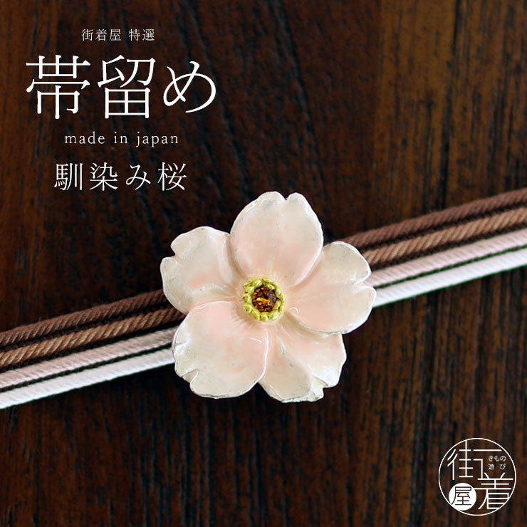A pink cherry-blossom clip for a kimono obi belt placed on layered obi cords on a wooden surface.