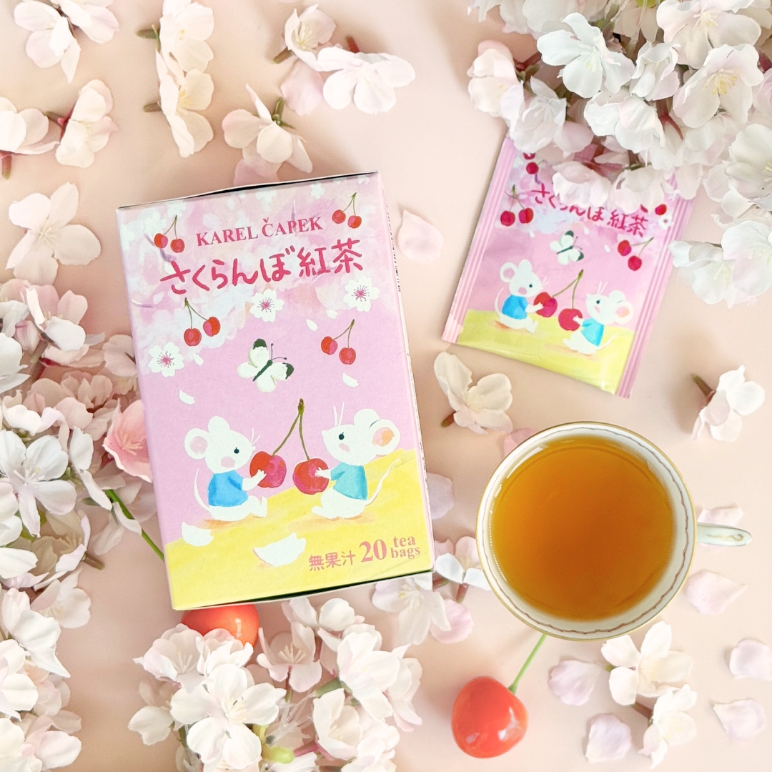 A pink box and single sachet of cherry tea next to a cup of brewed black tea and decorative cherry blossoms.