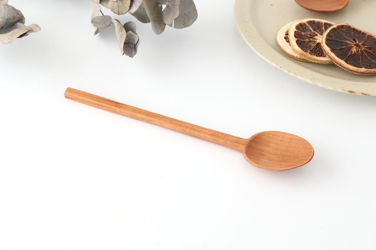 A cherry-wood curry spoon displayed on a white surface next to a plate and dried citrus slices.