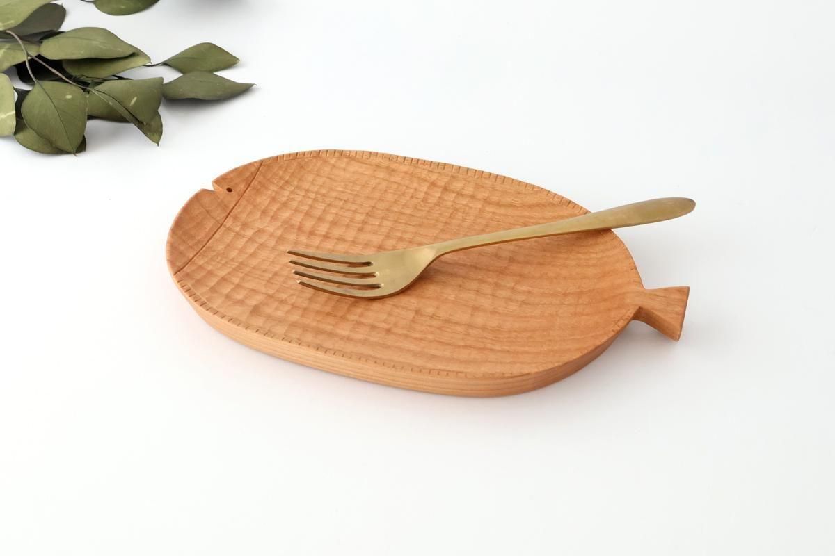 Wooden fish-shaped tray (cherry) on a white background with a brass fork and leaves nearby.
