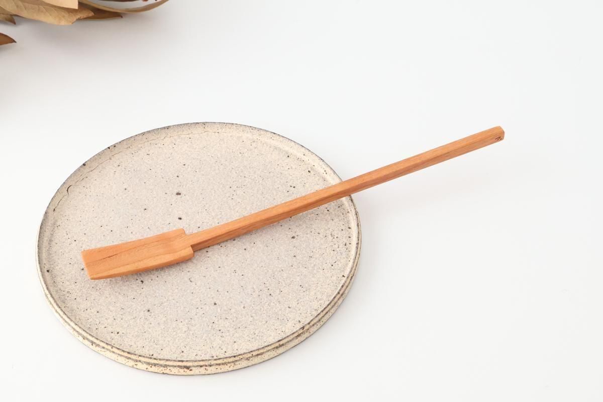 A cherry wood jam spoon laid on a round ceramic plate on a white background.