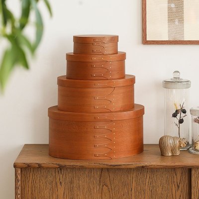 Stacked oval cherry wood Shaker-style storage boxes displayed on a wooden cabinet.