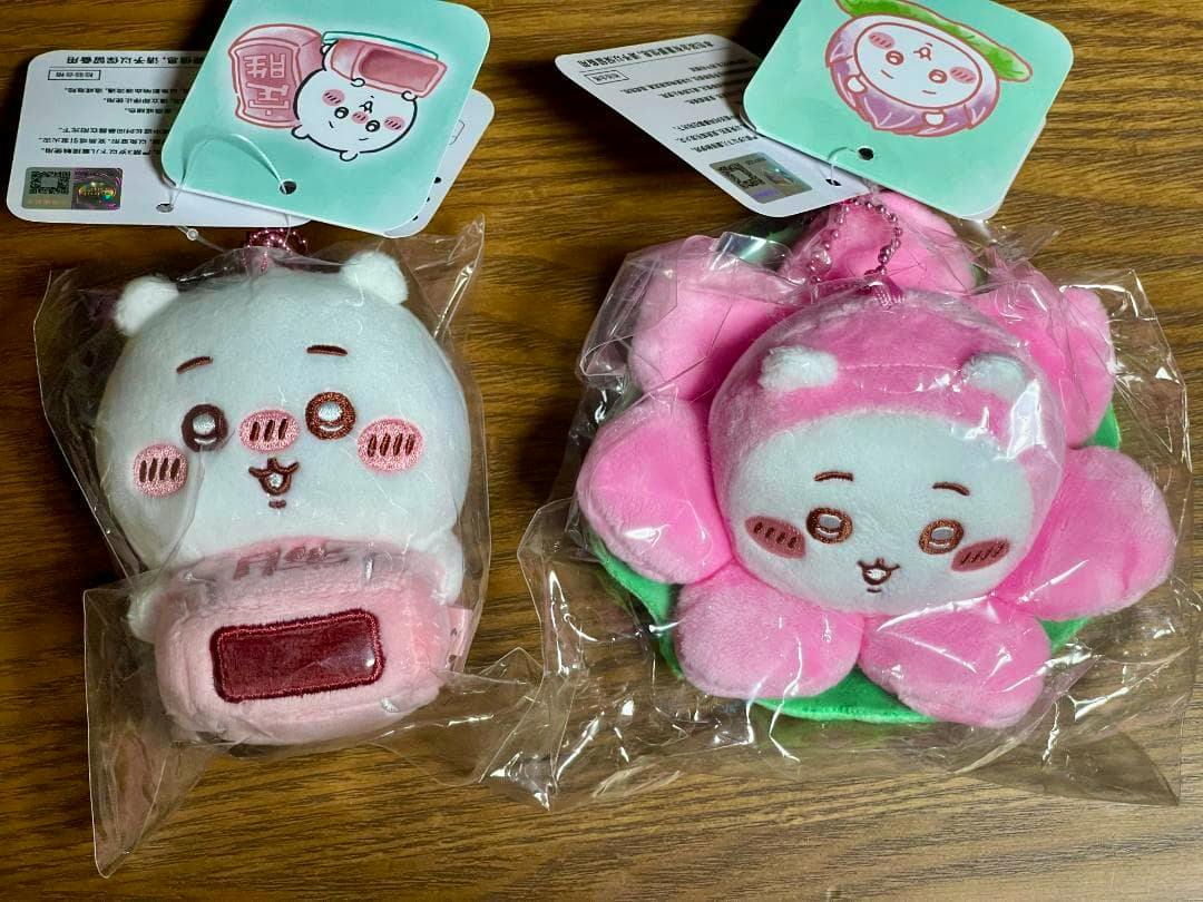 Two plush keychain toys (one white, one pink) in clear plastic packaging on a wooden surface.