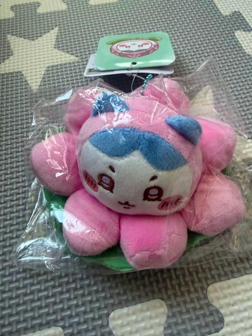 Pink lotus-flower Chiikawa mascot plush (ハチワレ) in clear plastic packaging with its tag visible.