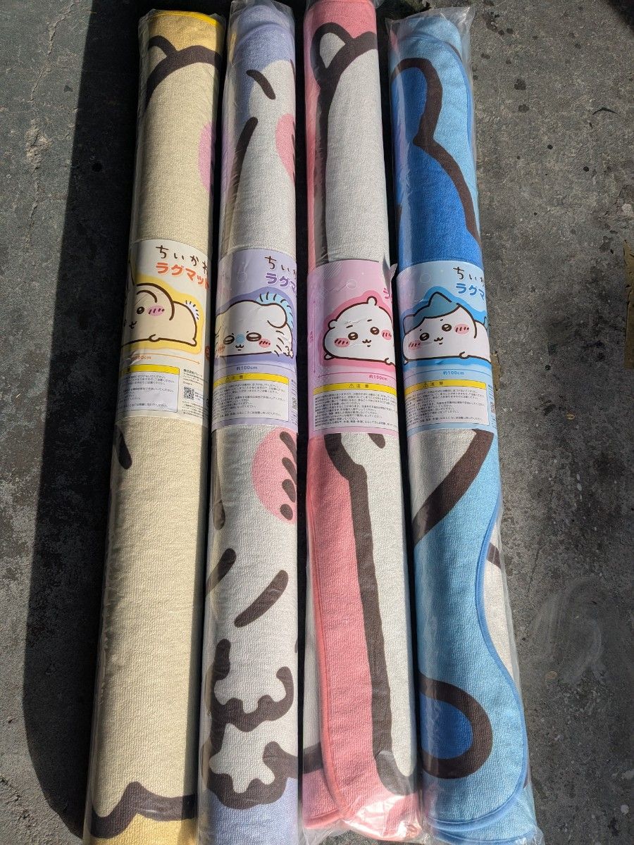 Four rolled, packaged ちいかわ floor mats in different colors arranged side by side.