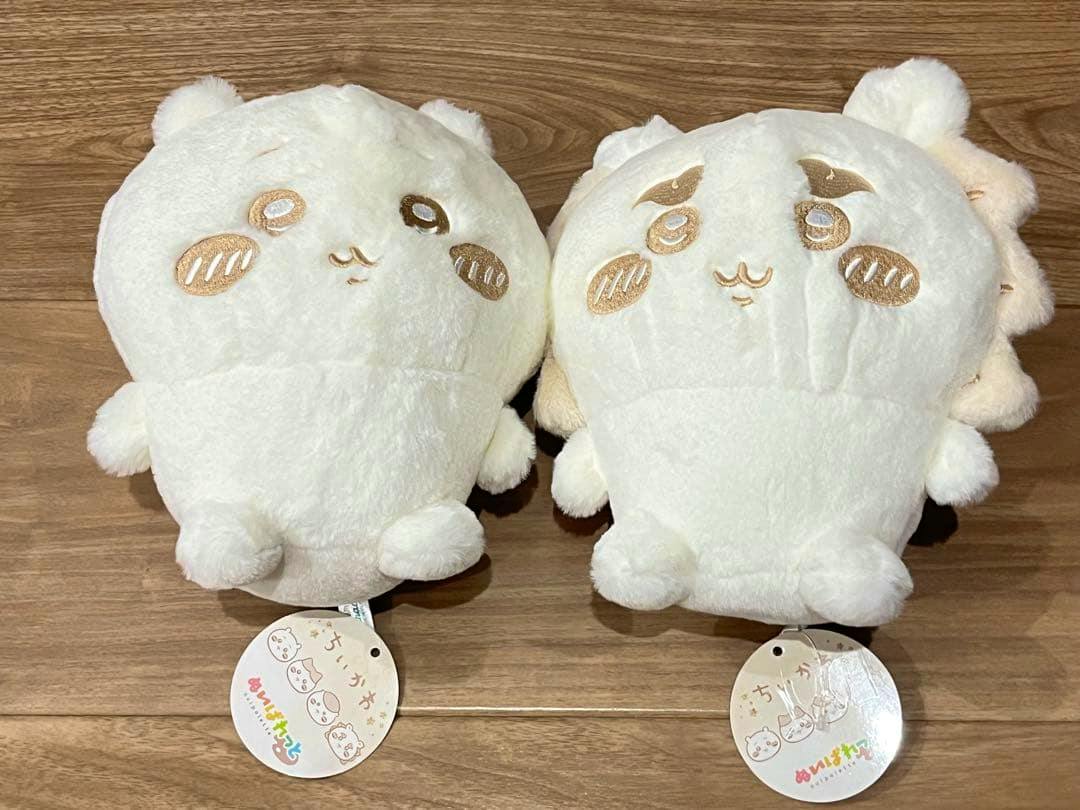 Two milk-colored Chikawa plush toys (2-piece set) shown from the front on a wooden floor with their tags visible.
