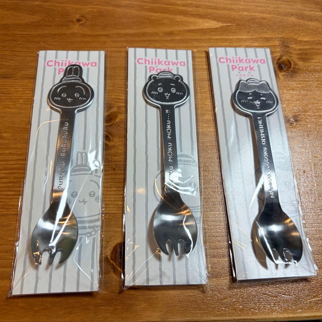 Three packaged Chiikawa Park stainless spoon-fork sets showing character faces on their handles on a wooden surface.