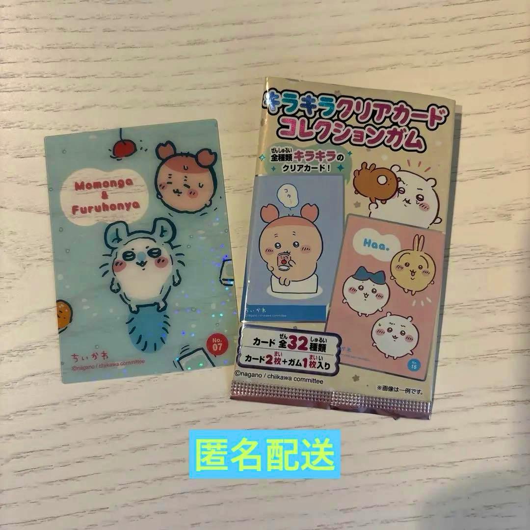 A clear collectible card depicting Momonga and Furuhonya shown next to its sealed pack on a light wood surface.